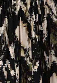 Zwarte en crèmekleurige stof met een patroon en groene accenten; heeft een getextureerd, abstract ontwerp en kleine knopen langs de voorkant.