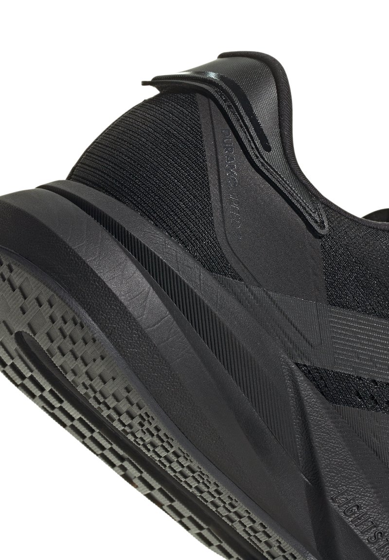 Scarpa sportiva nera con tomaia in maglia, suola in gomma testurizzata e silhouette elegante. Dettagli notevoli includono un linguetta posteriore e strisce a contrasto.