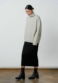 Lysegrå turtleneck sweater i oversized pasform, parret med en sort knælang blyantskirt og sorte blokhælede ankelstøvler.