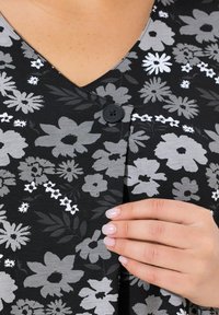 Czarna tkanina w kwiatowy nadruk z białymi i szarymi kwiatami, dekoltem w serek oraz czarnym guzikiem w pobliżu klatki piersiowej. Miękka tekstura.