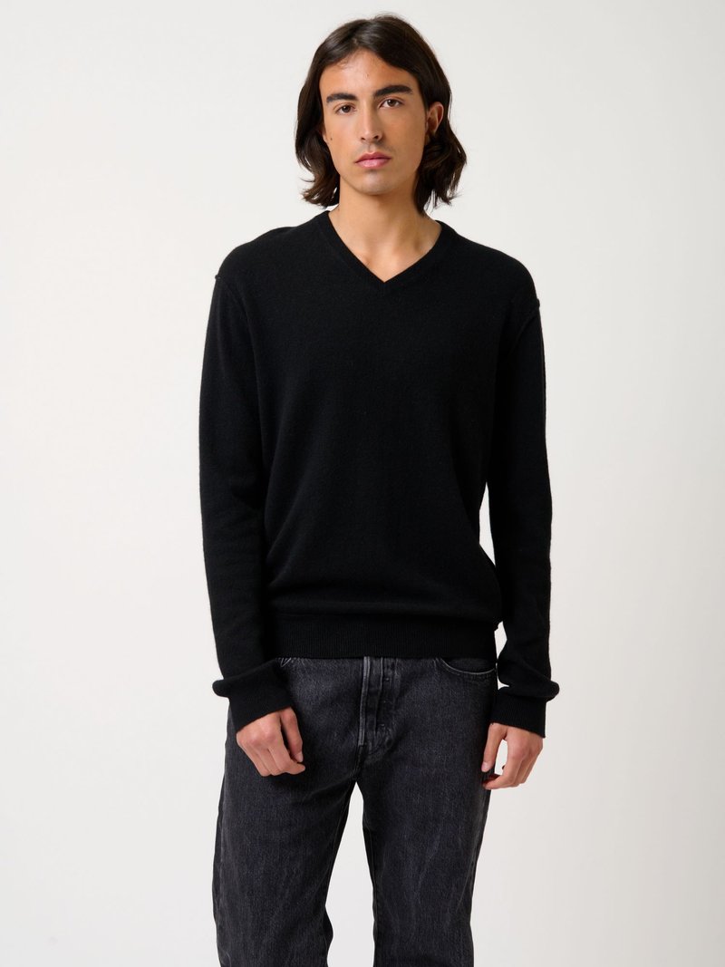 Schwarzer V-Ausschnitt-Pullover aus weichem Strickstoff, mit gerippten Bündchen und Saum, kombiniert mit dunklen Jeans. Einfaches, modernes Design.