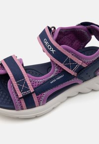 Lilla og marine sandaler med justerbare stropper, nett-detaljer, en polstret såle og en hvit gummisole merket "VANNSVENNLIG."