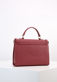 Czerwona skórzana torebka w ustrukturyzowanym kształcie. Posiada górny uchwyt, złote akcenty i teksturowaną powierzchnię. Widok z boku.