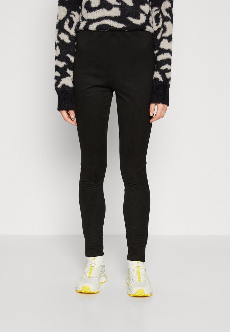 Black leggings made from stretchy material, featuring a slim fit and ankle length. Paired with light-colored athletic shoes.