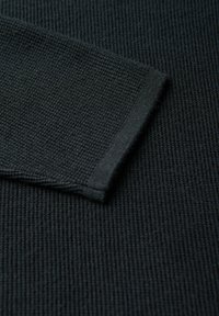 Dettaglio di un maglione di lana scuro che mostra una texture a coste e orli delle maniche rifiniti. Il materiale è morbido, con un pattern uniforme e un colore profondo.