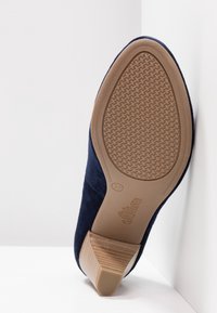 Chaussure en suede bleu marine avec une semelle en caoutchouc texturé et un talon empilé. La semelle extérieure présente un motif géométrique pour une meilleure adhérence. Taille 37.