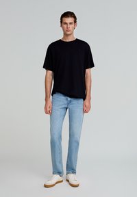 Sort T-shirt, afslappet pasform, korte ærmer. Lyseblå jeans, slim fit, falmet tekstur. Hvide sneakers med en tan gummisål.