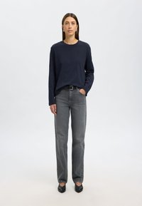 Tumesinise pika varrukaga särgi sobitamine hallide sirgete pükstega ja mustade tasapinnaliste kingadega, mis on lihtsa disaini, sujuva tekstuuri ja minimalismi stiiliga.