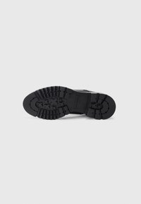 Suela de bota de goma negra con profundas estrías, punta redondeada y un logo en relieve. Presenta surcos para tracción y un diseño robusto.