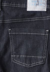 Tissu en denim foncé avec des coutures blanches, une poche arrière rectangulaire et une étiquette portant la mention "Simplicità". Texture lisse, design épuré.