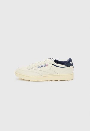 Baskets Reebok crème et bleu marine avec design à lacets, semelle en caoutchouc et logo de la marque sur le côté et le talon.