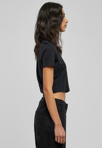 Svart avkortet t-skjorte med korte ermer. Myk stoff, enkel design, med rund hals og en rett hemline, kombinert med svarte bukser.