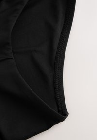 Fekete szövet közeli felvétele részletes varrással egy ívelt varrás mentén, világos háttéren.