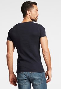 Granatowa koszulka z krótkim rękawem uszyta z elastycznej bawełny, dopasowany krój pokazujący widok z tyłu. Połączona z jasnoniebieskimi dżinsami.