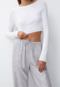 Haut blanc court à manches longues avec une texture côtelée, associé à un pantalon taille haute gris clair brillant avec une taille à cordon.