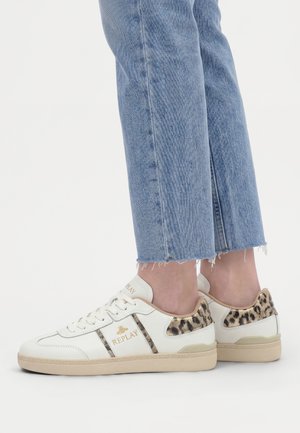 Baskets basses blanches avec des accents imprimé léopard, portées avec un jean bleu clair raccourci sur des chevilles nues.