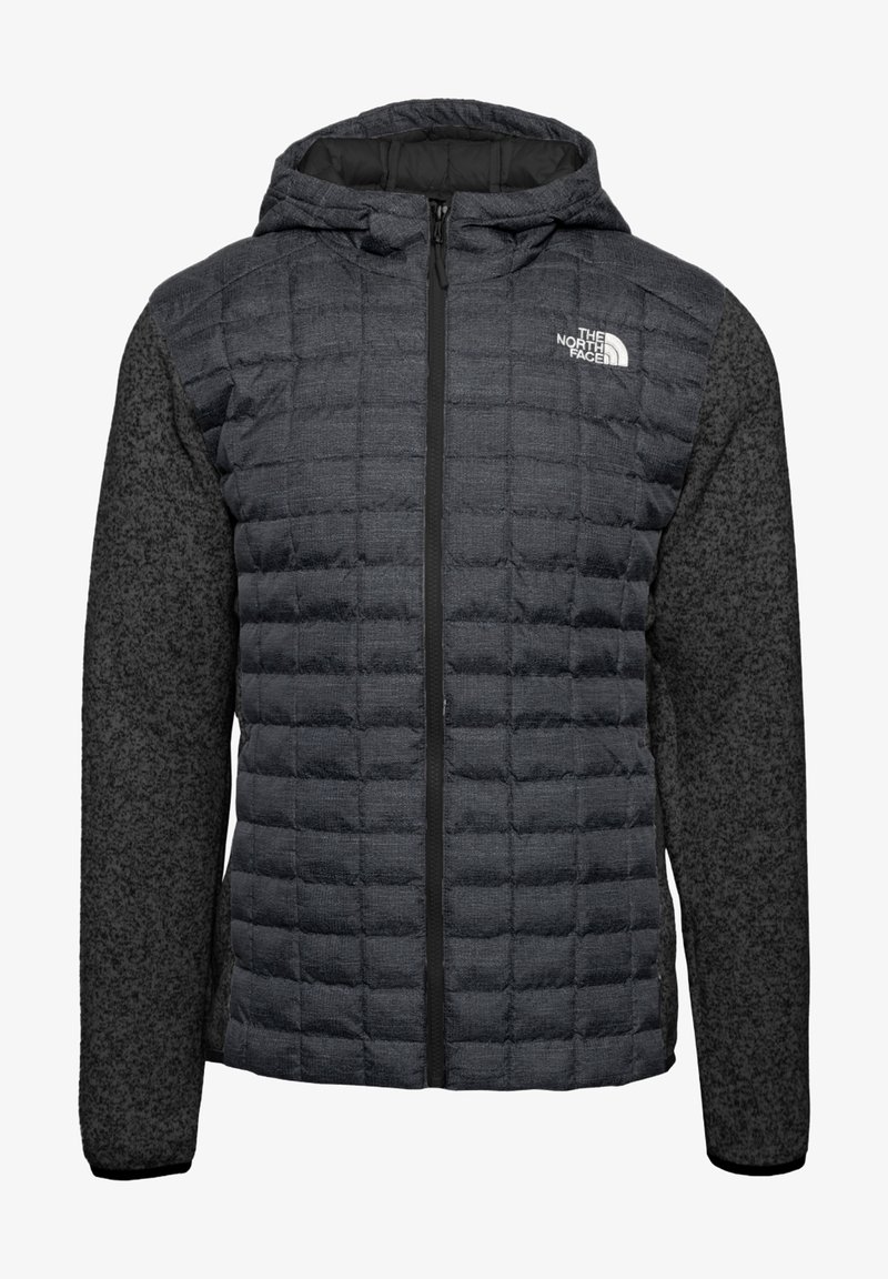 Puffjacka i mörkgrått med quiltad front, slät huva och kontrasterande texturerade ärmar. Har en svart dragkedja och logodetalj.