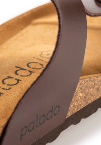 Sandal in pelle marrone con suola in sughero, plantare marrone texturizzato e una fascia marrone liscia con il logo "palado". Artigianato finemente dettagliato.