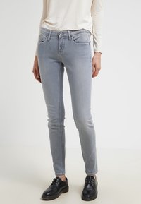 Světlé šedé slim džíny s pěti kapsami, poutky na opasek a viditelným šitím. Doplněné krémovým topem s dlouhým rukávem a černými botami.