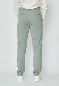 Pantalons tapered vert clair avec une ceinture confortable, deux poches arrière avec un subtil passepoil, et une texture de tissu lisse.