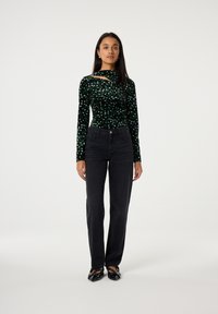 Zwarte jeans gecombineerd met een groen fluwelen top met lange mouwen, voorzien van een uitgesneden detail en een bloemmotief in verschillende tinten groen.