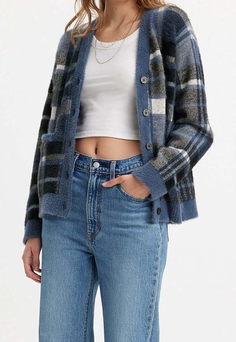 Karierte Strickjacke in Blau und Grau mit weicher Textur, Knöpfen und Taschen, kombiniert mit hoch geschnittenen blauen Jeans. Einfaches, lässiges Design.