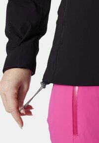 Černá sportovní bunda s detailem stažení na spodním lemu. Rukáv má texturované logo. Spárováno s růžovými kalhotami, které mají lesklý zip.