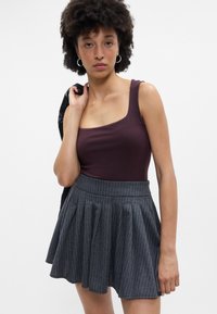 Μπορντό μπλούζα χωρίς μανίκια με τετράγωνη λαιμόκοψη, συνδυασμένη με γκρι φούστα με ρίγες και πτυχώσεις, διαθέτοντας εφαρμοστό ζωνάκι και φαρδύ στρίφωμα.