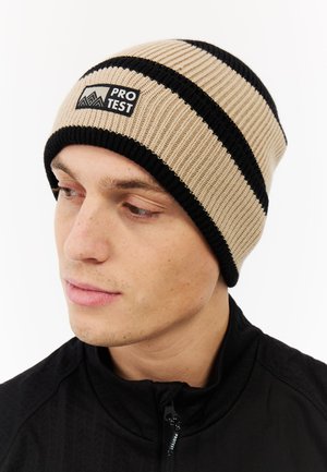 Knitted beanie in beige and black stripes, featuring a logo patch, close-fitting design, and ribbed texture.