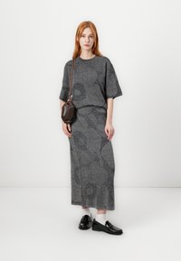 Sivý pletený outfit pozostávajúci z topu s krátkym rukávom a dlhej sukne, s jemnými vzormi. Skombinovaný s čiernymi loafers a hnedou taškou.