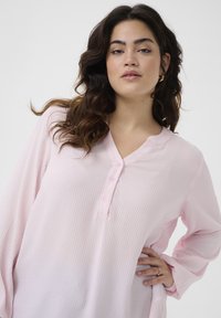 Top de manga larga rosa claro con textura de gofre, escote en V y tres botones. Presenta mangas relajadas y un ajuste holgado.