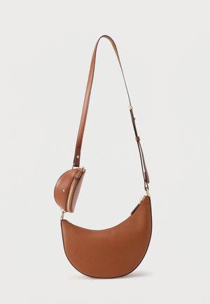 Sac à bandoulière en cuir marron en forme de croissant avec une sangle ajustable et une petite pochette à monnaie attachée avec une fermeture éclair sur un fond uni.