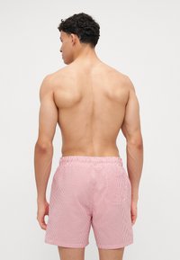 Κόκκινες και λευκές ριγέ μαγιό σορτς από ελαφρύ ύφασμα, με ελαστική μέση και μία πίσω τσέπη.