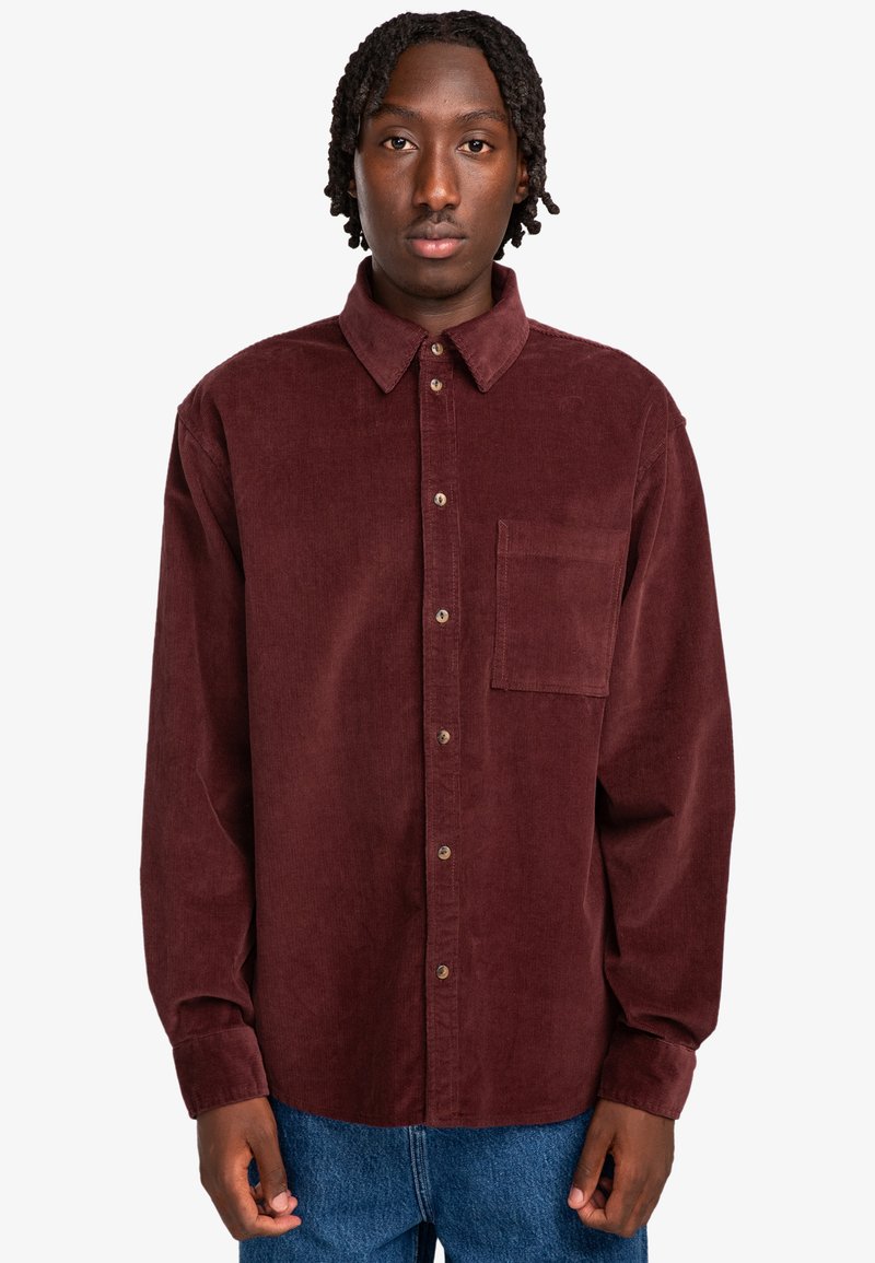 Camisa de pana burdeos con cuello abotonado, bolsillo frontal y botones marrones. Mangas largas y corte relajado. Sin patrones visibles.
