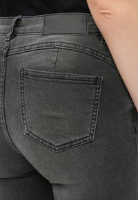 Μαύρα τζιν με πίσω τσέπη που διαθέτει διακριτό σχέδιο ραψίματος. Η ζώνη περιλαμβάνει μια μαύρη δερμάτινη ετικέτα που αναγράφει «NOISY MAY».}}}]}