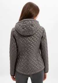 Grau gesteppte Jacke mit Kapuze, die über ein tailliertes Design und ein strukturiertes Muster verfügt. Das Material wirkt leicht und isolierend.