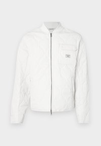 Balta dygsniuota striukė su užtrauktuku priekyje, ribiniu apykakle ir vienu krūtinės kišeniu su logotipo ženkliuku. Glotni tekstūra ir minimalistinis dizainas.