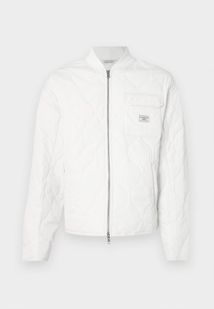 Fehér steppelt dzseki cipzáros elejjel, bordázott gallérral és egyetlen mellzsebbel, melyen logós címke látható. Simogató tapintású, letisztult dizájn.