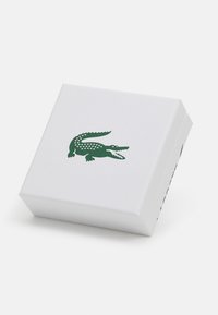 Bijela kutija s teksturom s zelenim logotipom krokodila na vrhu, s čistim linijama i jednostavnim dizajnom.