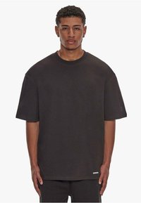 Overmaat zwart katoenen t-shirt met een ronde hals, korte mouwen en subtiele logodetail aan de zoom. Zachte textuur en recht gesneden ontwerp.