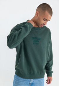 Donkergroene sweatshirt van zacht materiaal, met een ronde hals, ribgebreide manchetten en een geborduurd ontwerp "BROOKLYN 1993 NEW YORK".