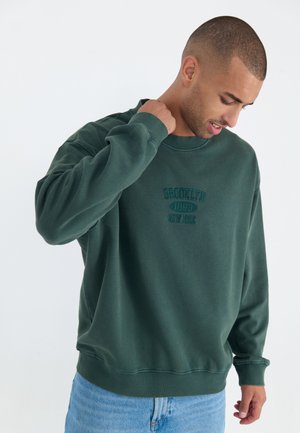 Donkergroene sweatshirt van zacht materiaal, met een ronde hals, ribgebreide manchetten en een geborduurd ontwerp "BROOKLYN 1993 NEW YORK".