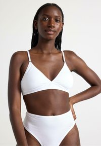 Vit bomullsbralette med justerbara axelband och triangelformade kupor, kombinerad med vita bikinitrosor med hög midja, slät textur.