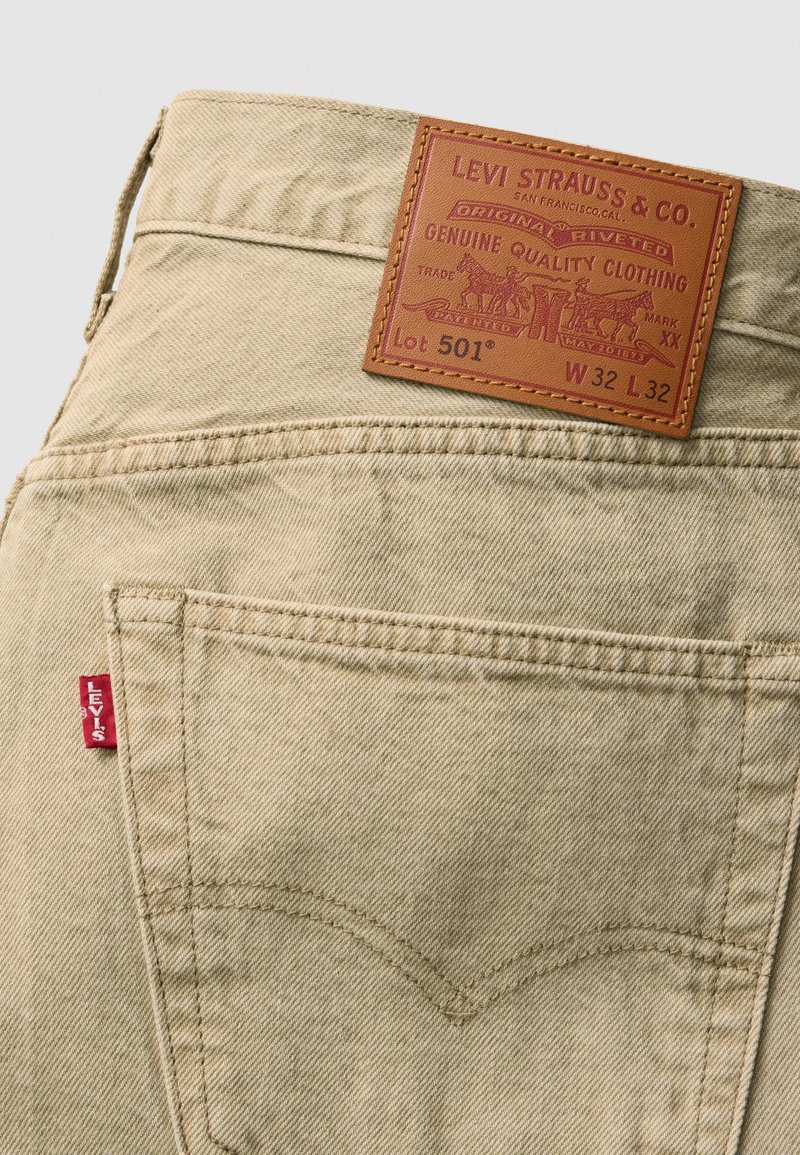 Beige Denim-Jeans mit Gesäßtaschen, featuring ein braunes Lederpatch mit der Aufschrift "LEVI STRAUSS & CO." und einem roten Tab an der Seitennaht.