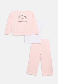 Ροζ φούτερ με στρογγυλεμένη ραφή, λευκό T-shirt και ταιριαστό ροζ παντελόνι. Το φούτερ έχει μαύρο κείμενο «KARL LAGERFELD PARIS» στην πλάτη.