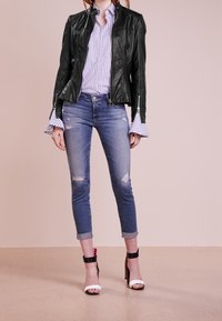 Černá kožená motorkářská bunda se zipy na ramenech, bílá a modrá pruhovaná košile, oprané modré skinny džíny, černé a bílé sandály na vysokém podpatku.