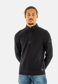 Maglione navy a maglia con colletto alto e mezza patta, caratterizzato da un tessuto strutturato e toppe a contrasto sulle maniche.