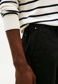 Maglione a righe di colore crema e blu navy, con polsini a costine; abbinato a pantaloni neri con un piccolo dettaglio logo rosso, bianco e blu.