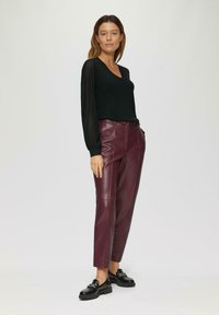 Un pull noir avec des manches texturées, associé à un pantalon en cuir bordeaux et des mocassins noirs, créant une tenue moderne et élégante.