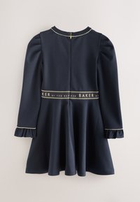 Diepblauwe jurk met pofmouwen, geplooide rok en gerimpelde manchetten. Voorzien van een gouden logoband in de taille en een achterritssluiting.